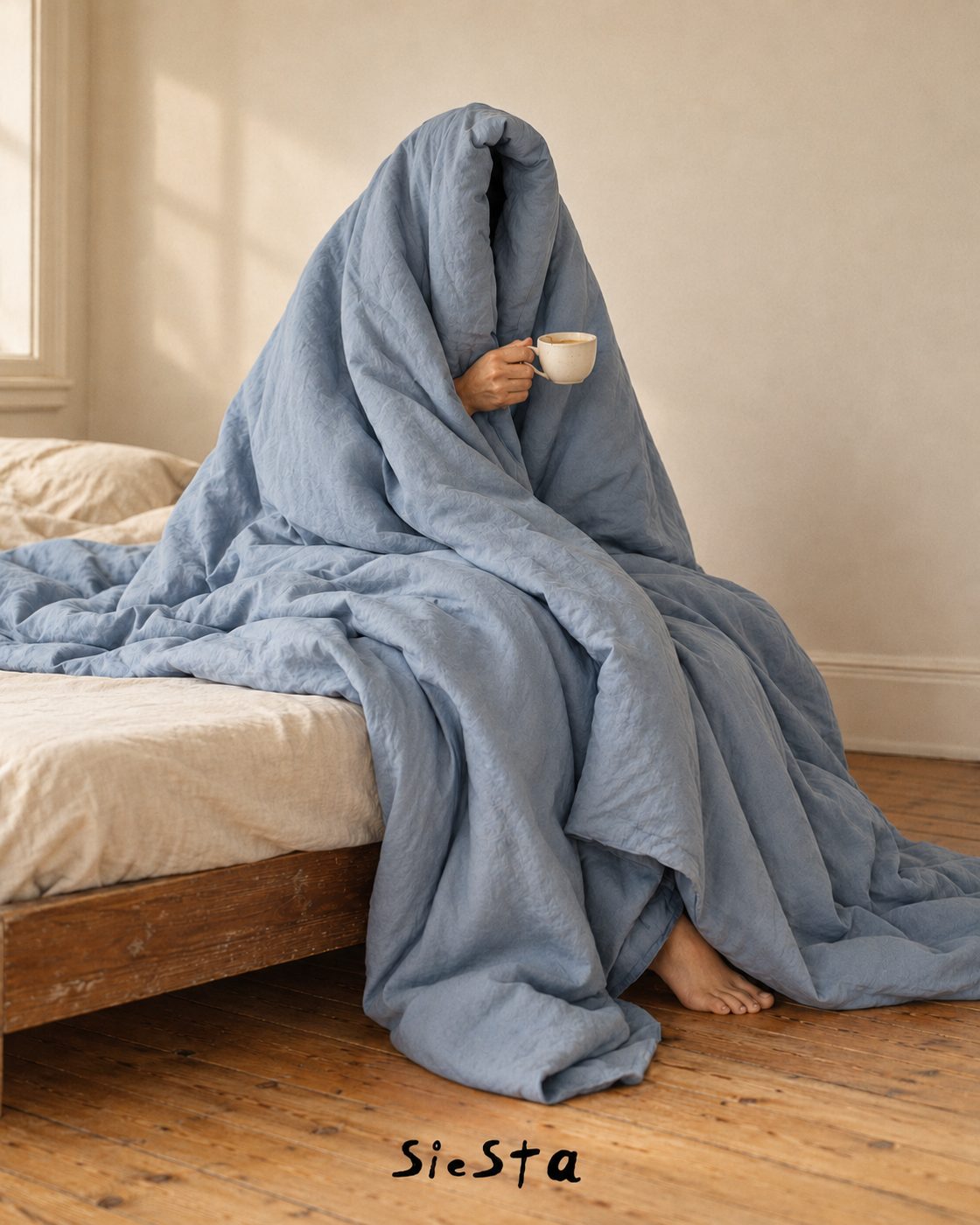 Person wrapped in a blue Siesta duvet holding a coffee